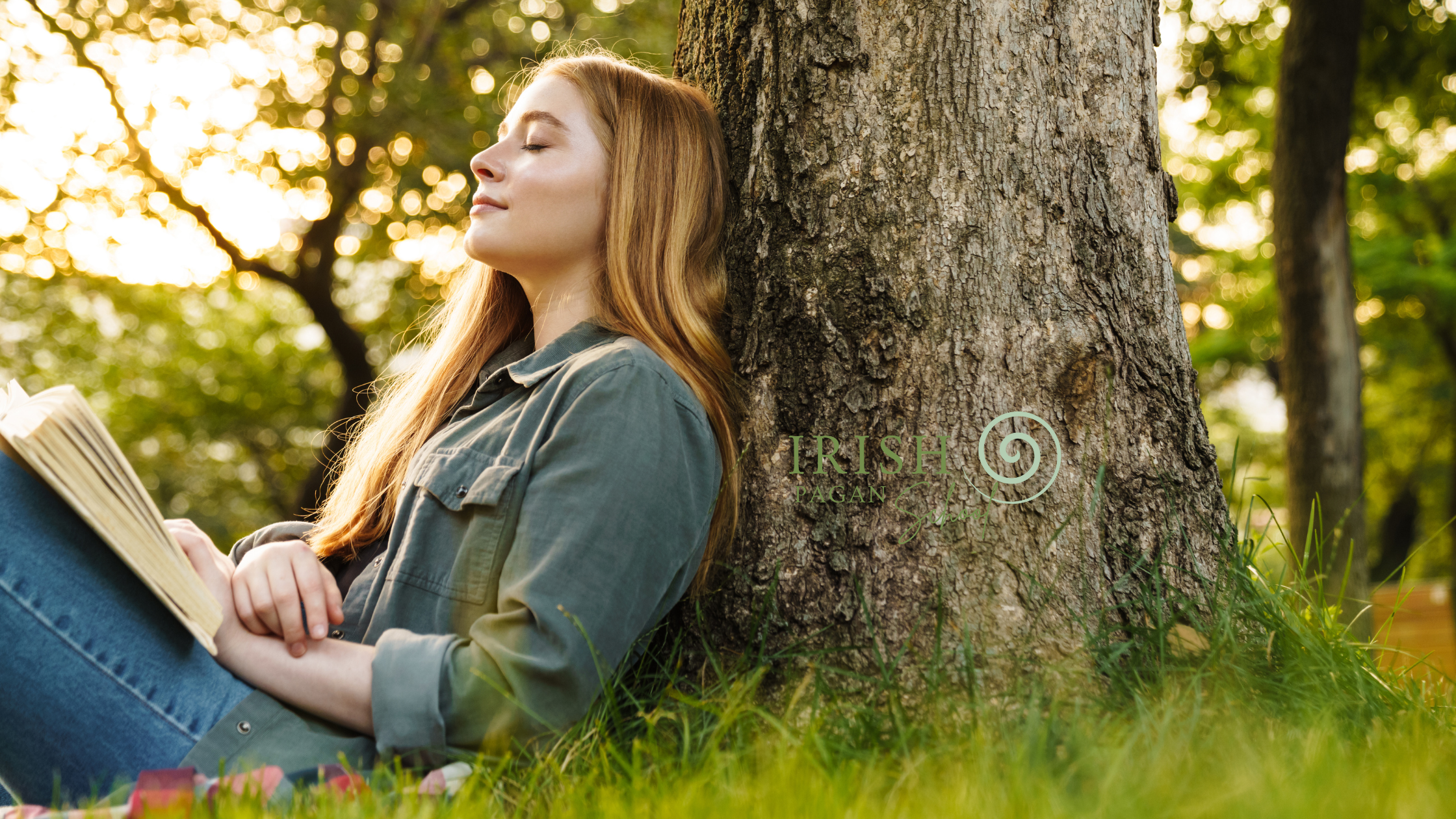 A young woman with long red hair sits peacefully against a tree in a sunlit forest, holding an open book. She has her eyes closed, embracing a moment of connection with nature. The Irish Pagan School logo is subtly placed on the tree trunk beside her.